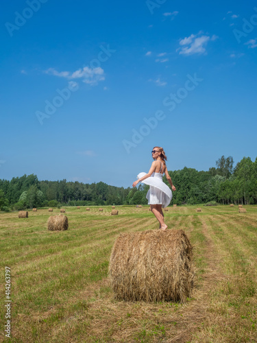 Girl dancing on a bale of hay on a summer day