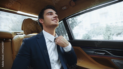 Relaxed male ceo sitting in comfortable car afterwork. Business man fixing tie © stockbusters