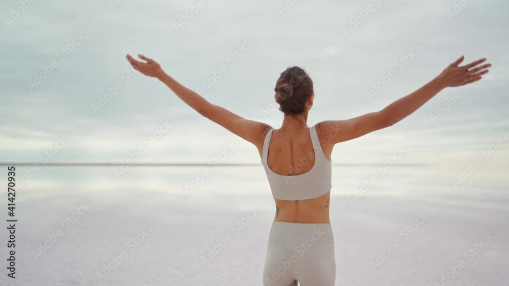 Woman with arms raised on deserted endless coast of mineral salt lake looking at Sunrise view. Hiker Girl lifting arm up celebrating life scenic nature landscape enjoying vacation travel adventure Woman with arms raised on deserted endless coast of mineral salt lake looking at Sunrise view. Hiker Girl lifting arm up celebrating life scenic nature landscape enjoying vacation travel adventure