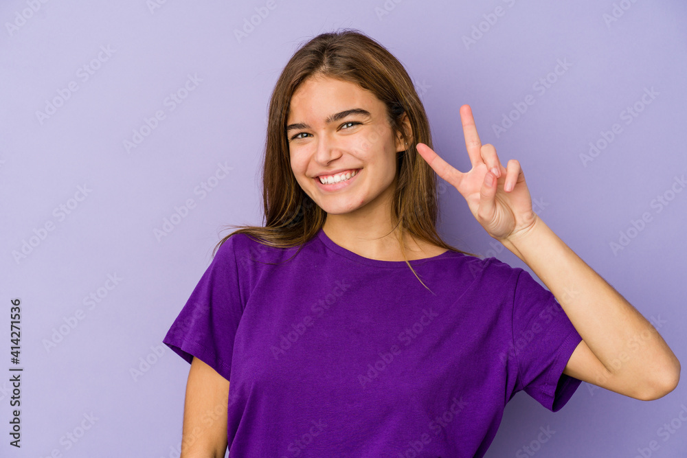 Young skinny caucasian girl teenager on purple background joyful and carefree showing a peace symbol with fingers. Young skinny caucasian girl teenager on purple background joyful and carefree showing a peace symbol with fingers.