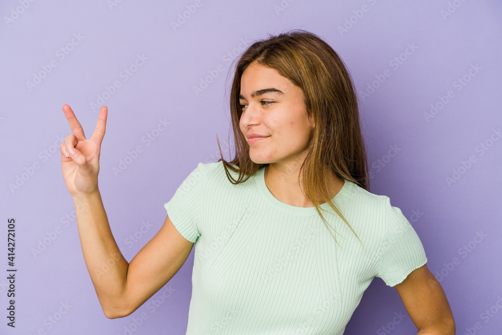 Young skinny caucasian girl teenager on purple background joyful and carefree showing a peace symbol with fingers. Young skinny caucasian girl teenager on purple background joyful and carefree showing a peace symbol with fingers.