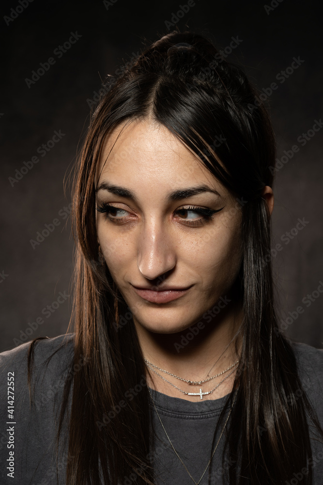 Joven modelo caucásica de pelo castaño oscuro, guapa, en fondo gris oscuro, mirando maliciosamente hacia un lado
