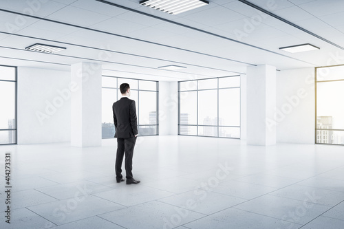 Businessman in black suit in empty spacious hall room with light walls, big windows