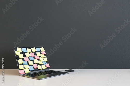Opened laptop with colored remider sticks on display on light empty table at dark wall background photo