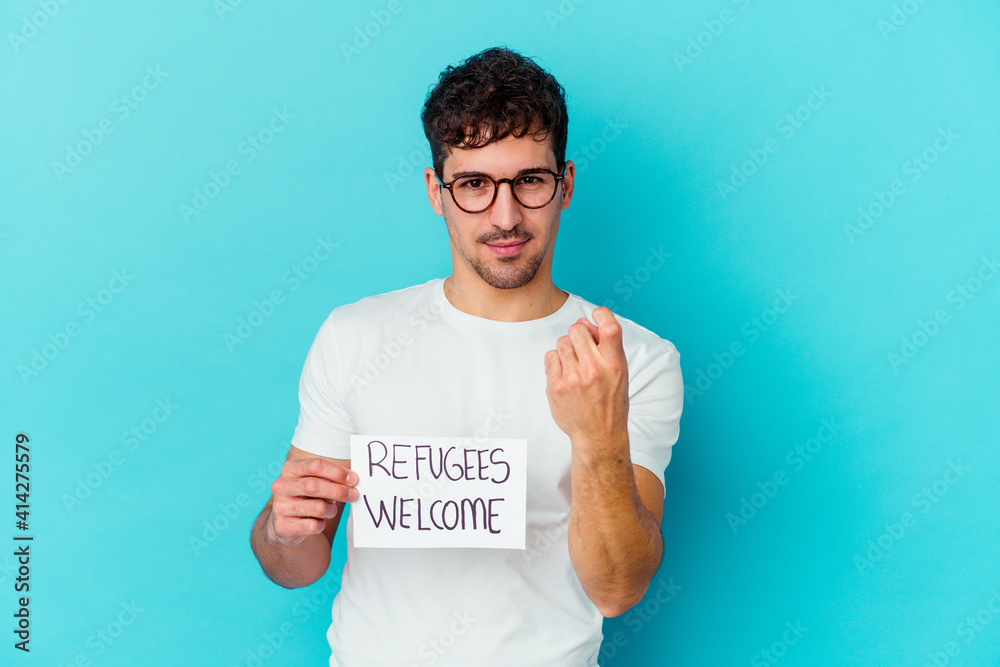 Young caucasian man holding a Refugees welcome placard isolated pointing with finger at you as if inviting come closer. Young caucasian man holding a Refugees welcome placard isolated pointing with finger at you as if inviting come closer.