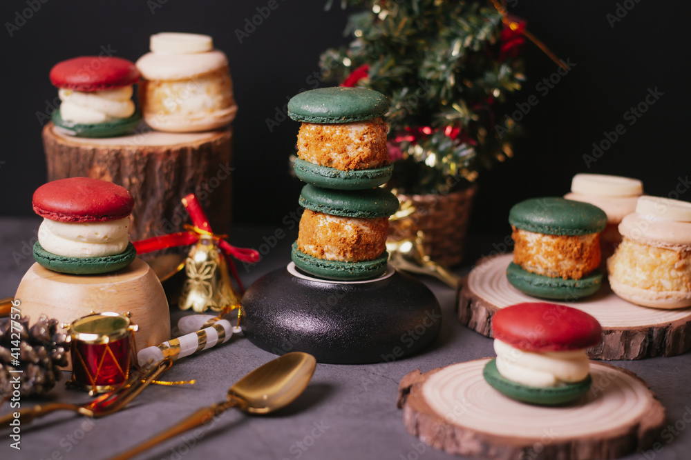 red macaroon,white macaroon,green macaroon on the wood plate with christmas tree on dark background red macaroon,white macaroon,green macaroon on the wood plate with christmas tree on dark background