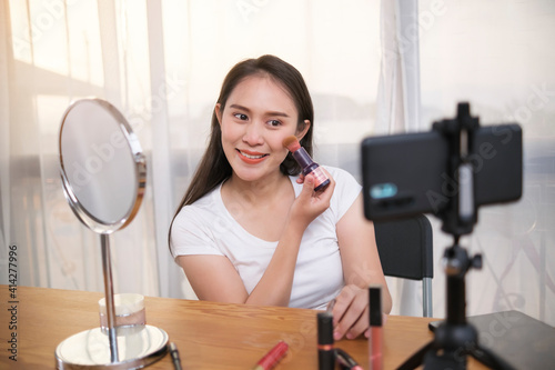 Young Asian woman video vlogger video recording tutorial live stream broadcasting on social media, content creator influencer happy smiling sales advertisement online product, at home using smartphone