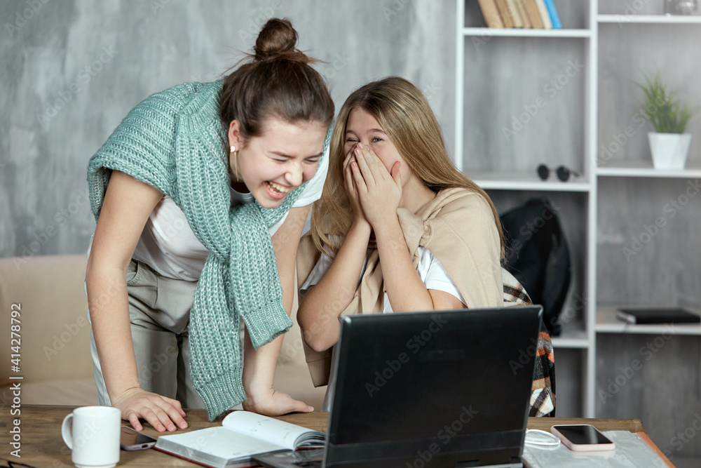 Two cute young students looking at a laptop, laughing and having fun, chatting gossip on the Internet. The friendship of two girls. Two cute young students looking at a laptop, laughing and having fun, chatting gossip on the Internet. The friendship of two girls.
