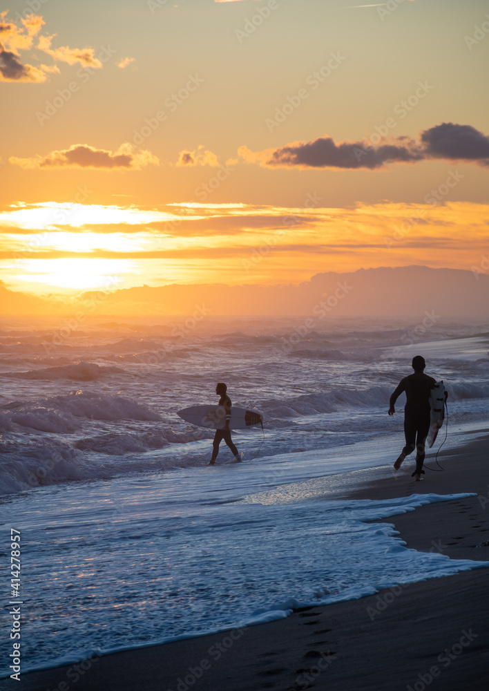 Surfers on the beach running during the sunset Surfers on the beach running during the sunset