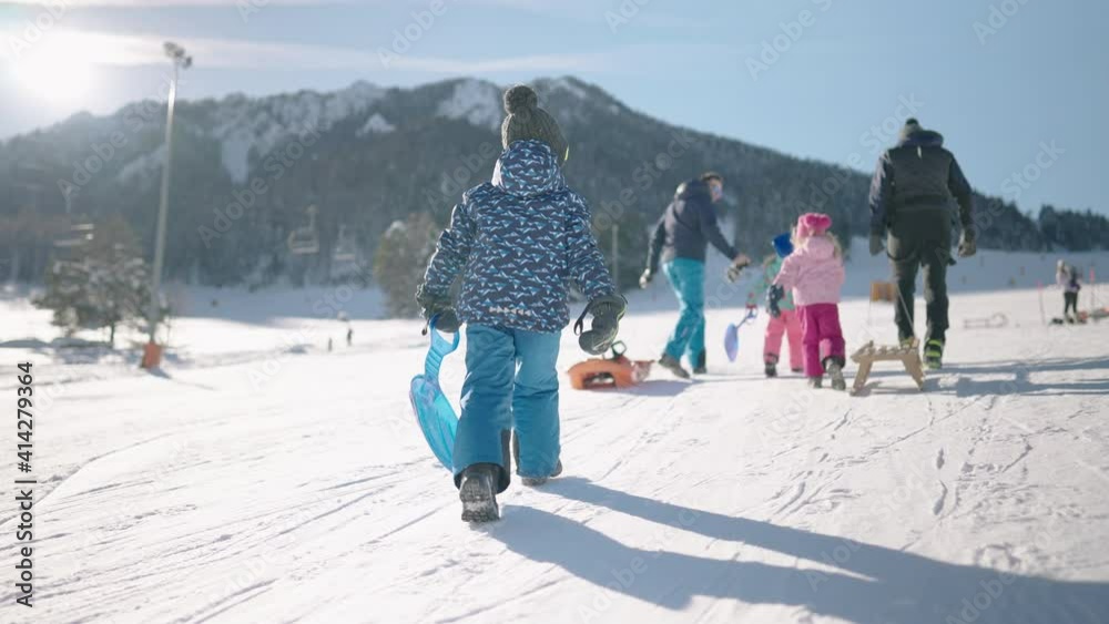 Slow motion - Family walking uphill with snow sleds to go sledging. Parents and children having winter fun outdoors