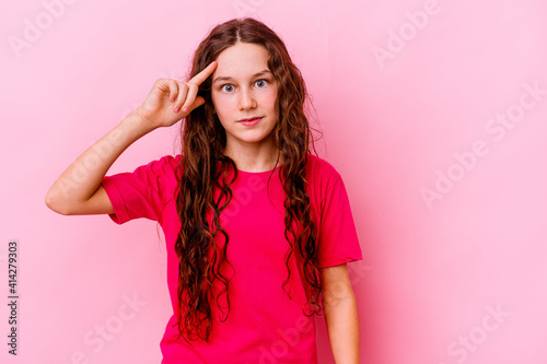 Little caucasian girl isolated on pink background pointing temple with finger, thinking, focused on a task.