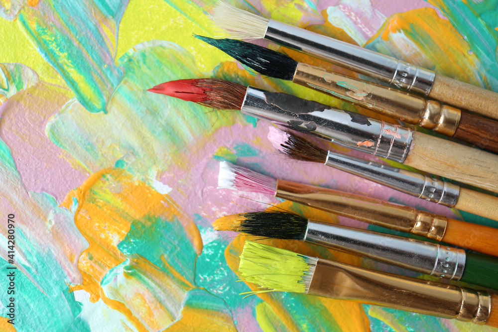 Obraz premium Set of different brushes on abstract colorful paint, flat lay