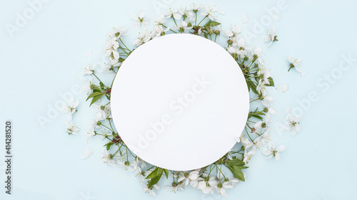 Round frame with spring flowers. Flowers on cherry tree branches in form of wreath on blue background. Leaf pattern. Flat lay, top view, copy space. Mockup