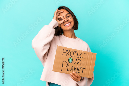 Young hispanic mixed race woman holding a protect our planet cardboard excited keeping ok gesture on eye. © Asier