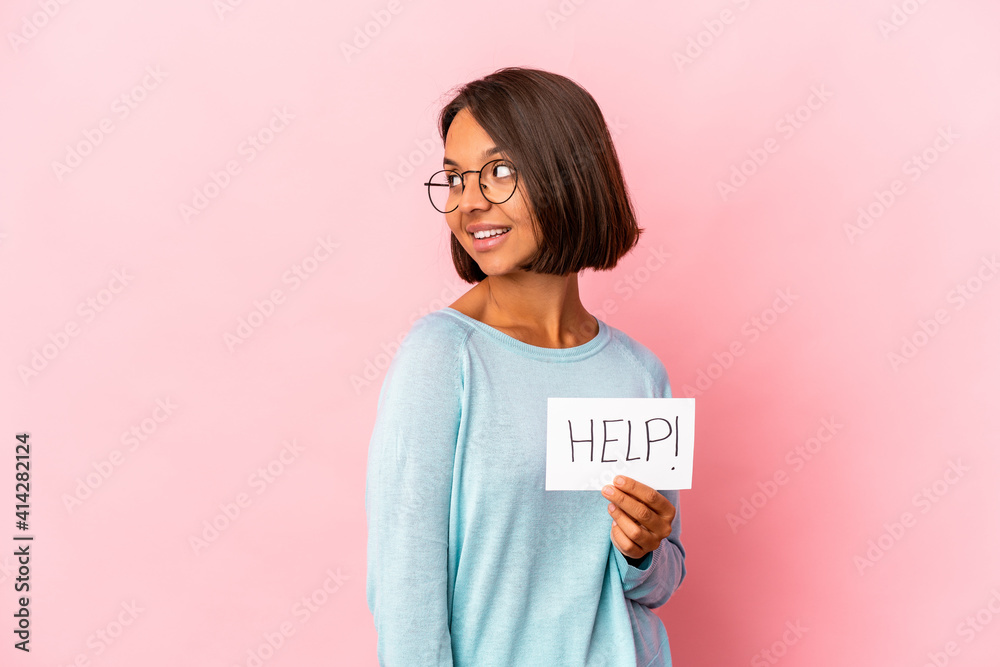 Young hispanic mixed race woman holding a help poster looks aside smiling, cheerful and pleasant. Young hispanic mixed race woman holding a help poster looks aside smiling, cheerful and pleasant.