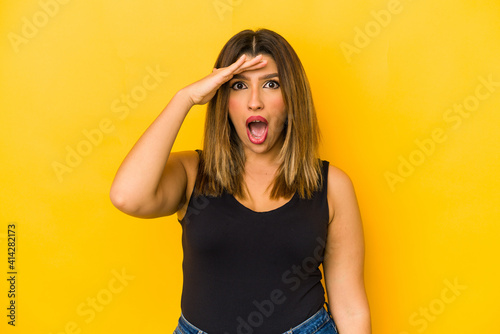 Young indian woman isolated on yellow background shouts loud, keeps eyes opened and hands tense.