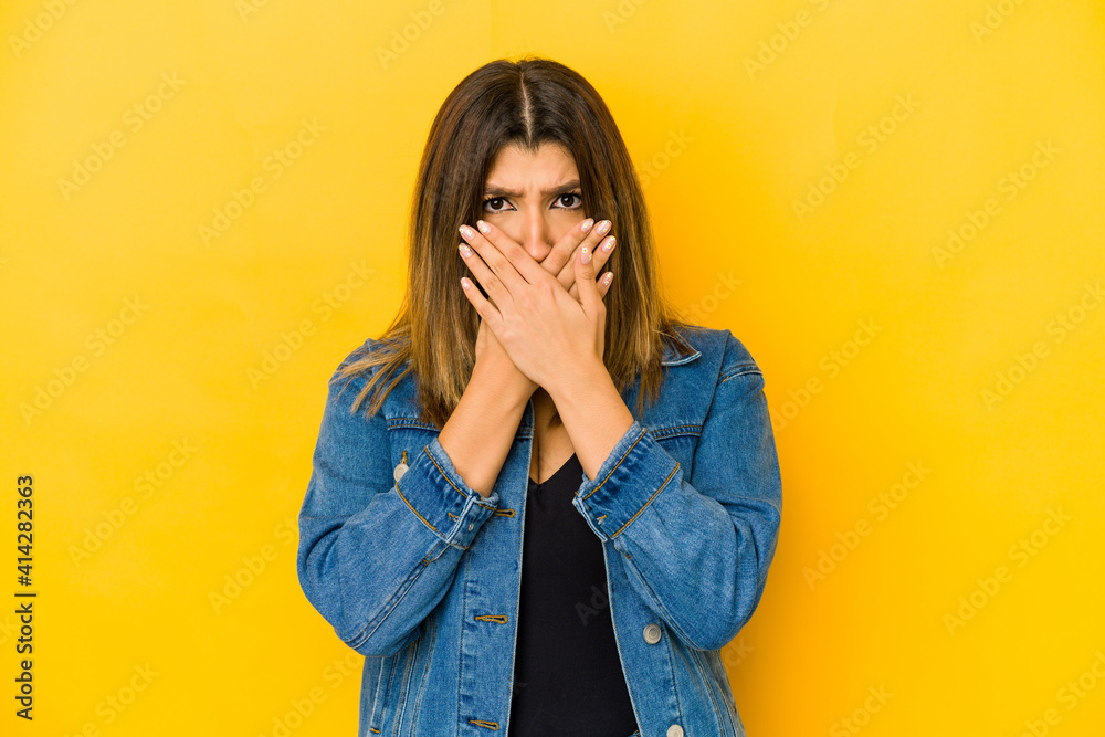 Young indian woman isolated on yellow background covering mouth with hands looking worried. Young indian woman isolated on yellow background covering mouth with hands looking worried.