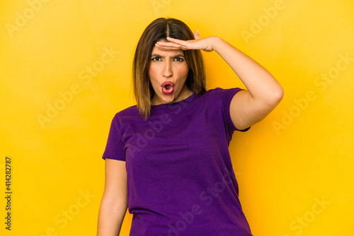 Young indian woman isolated on yellow background looking far away keeping hand on forehead. © Asier