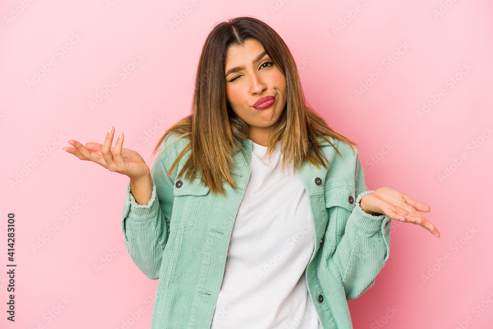 Young indian woman isolated on pink background doubting and shrugging shoulders in questioning gesture. Young indian woman isolated on pink background doubting and shrugging shoulders in questioning gesture.