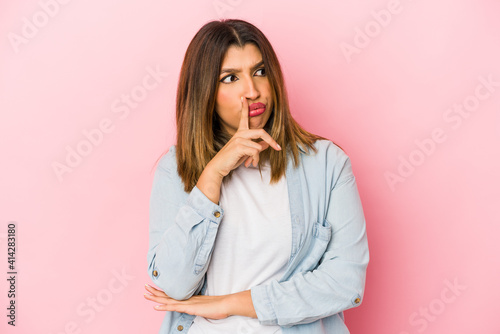 Young indian woman isolated on pink background looking sideways with doubtful and skeptical expression.
