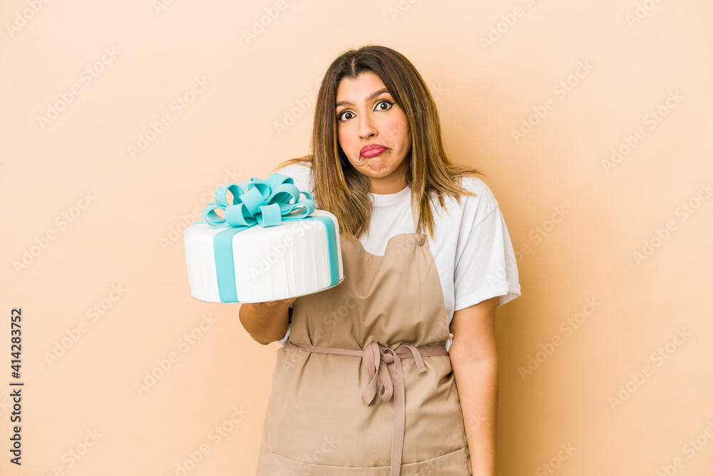 Young indian pastry chef woman isolated shrugs shoulders and open eyes confused.