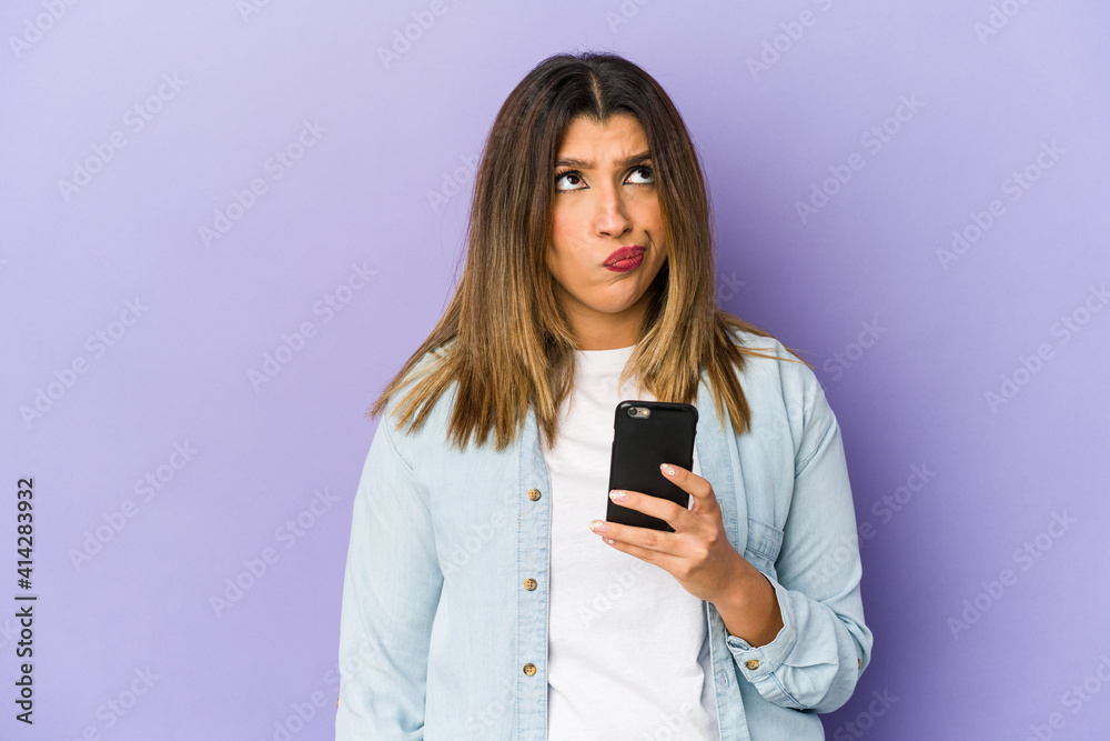 Young indian woman holding a phone isolated confused, feels doubtful and unsure. Young indian woman holding a phone isolated confused, feels doubtful and unsure.