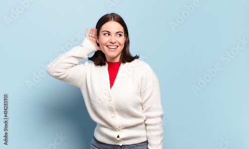 young pretty casual woman smiling, looking curiously to the side, trying to listen to gossip or overhearing a secret photo