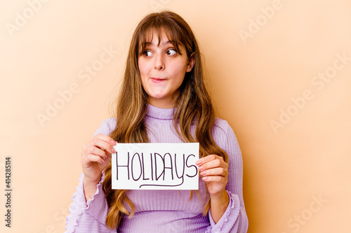 Young caucasian woman holding a Holidays placard isolated confused, feels doubtful and unsure.