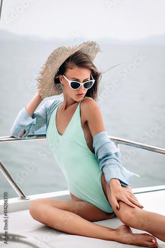 Passionate fit woman, wearing blue tight bikini, panama and white sunglusses is looking from bottom to top through the glasses