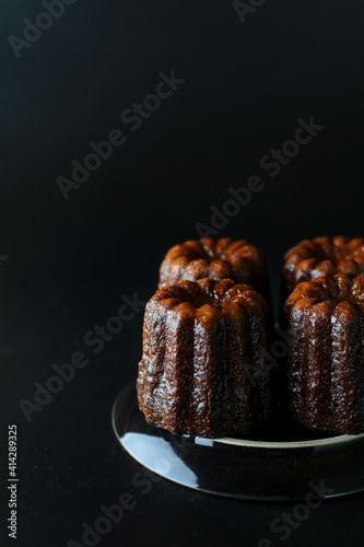 Caneles de bordeaux - traditional French sweet dessert serve with tea or coffee in dark tone on black background.