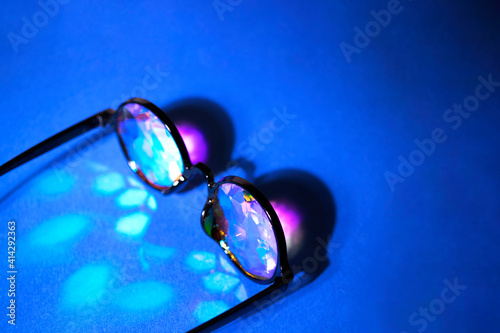 The kaleidoscope glasses in the black frame in the rays of light on a blue background. There is space for text.