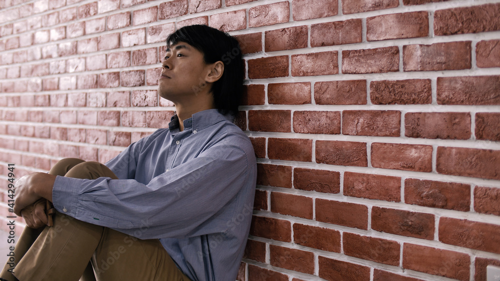 Obraz premium Depressed young man sitting on floor against a wall