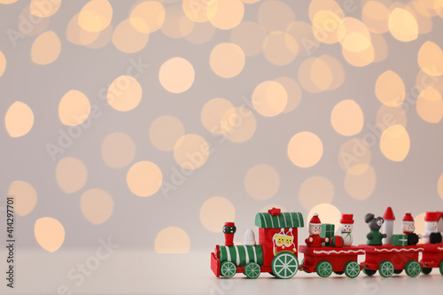 Toy train on white table against Christmas lights. Space for text
