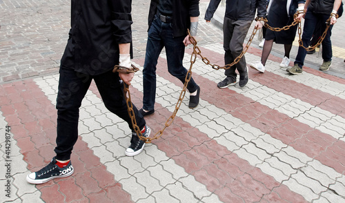 people with chain on hands of chained together are walking and cross over red lines of crosswalk on a street