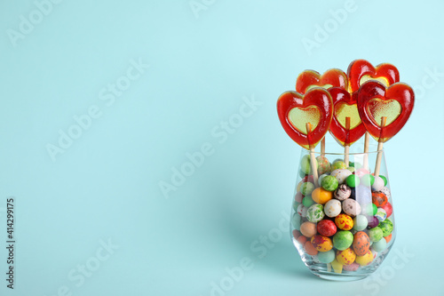 Delicious heart shaped lollipops and dragees in glass on turquoise background. Space for text