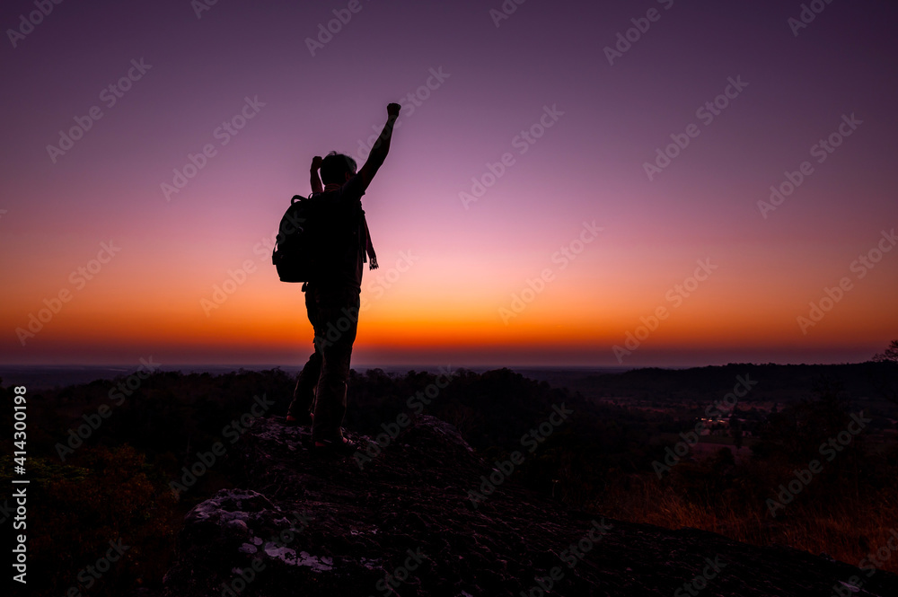 Silhouette of man standing a lone on top of mountain with orange sunrise in the morning light from the back and show two hands.Concept to create energy and positive thinking.