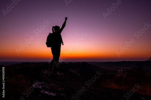 Silhouette of man standing a lone on top of mountain with orange sunrise in the morning light from the back and show two hands.Concept to create energy and positive thinking.
