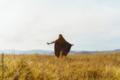 on the yellow grass of the steppe towards the hills runs a girl in a cape to the toe. High quality photo
