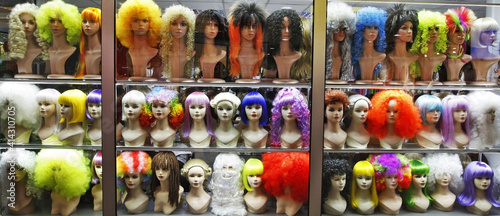 lots of multicolored female wigs on mannequin heads in a shop window 