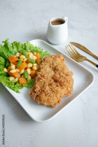crispy chicken steak with vegetables in a white plate served with sauce against white background