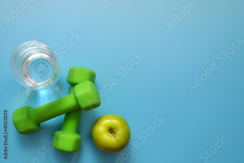 Dumbbells with an apple on a beige background. Sports and a healthy lifestyle in the modern world