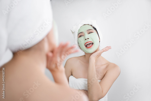 Asian woman use a facial mask. She is looking in the mirror.