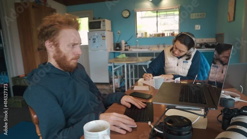 Work from home couple sits in an open plan kitchen at a large cluttered table in winter.
