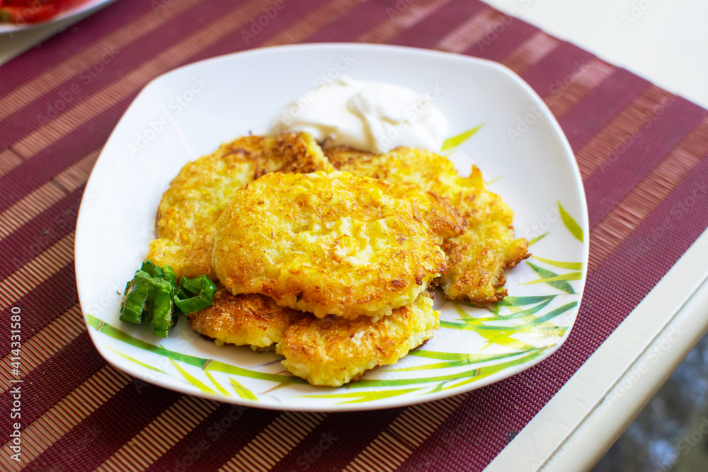 Appetizing zucchini pancakes with herbs on a white plate on the table. Appetizing zucchini pancakes with herbs on a white plate on the table.