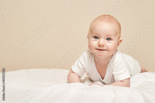 Cute small boy lying at bed. Childhood concept. Light background. Smiling child. Happy emotion. Copyspace. Stay home. Mockup. White clothes