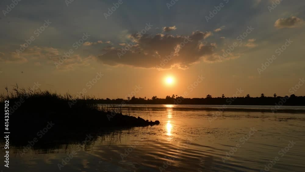Time lapse of tropical river bank at dusk sunset with clouds in orange sky