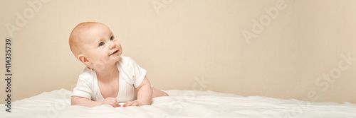 Cute small boy lying at bed. Childhood concept. Light background. Smiling child. Happy emotion. Copyspace. Stay home. Mockup. Horizontal banner. White clothes