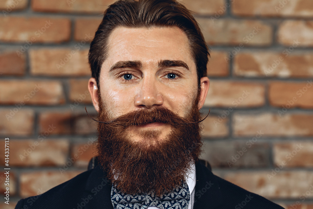Portrait of a charming satisfied man with a mustache and beard posing against a brick wall and grining. Emotion concept Portrait of a charming satisfied man with a mustache and beard posing against a brick wall and grining. Emotion concept