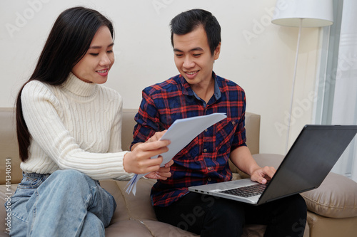 Young Asian couple entering infromation from document in form on laptop to get state service