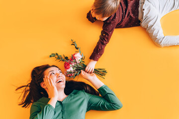 Little boy gives mom a bouquet of flowers against a yellow background. Gift for womens day and mothers day, top view.
